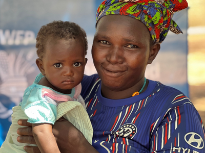 A woman looks into the camera and smiles while holding a baby 
