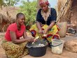 Two women kneel on the ground and prepare food
