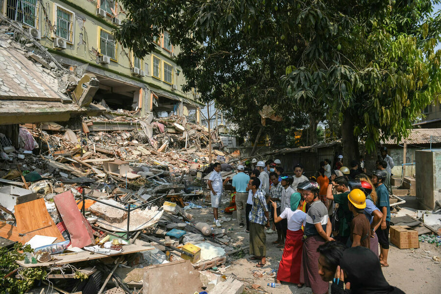 A small crowd of people walk past a building destroyed by an earthquake