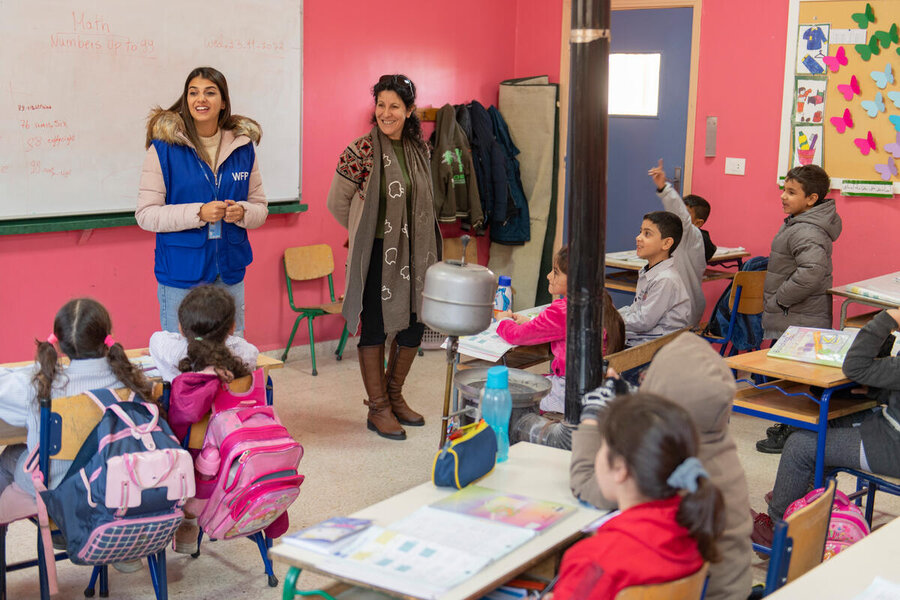 A woman in a WFP jacket addresses a class of young children as the teacher looks on