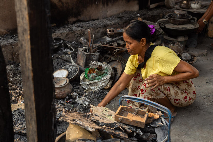 A woman in a yellow shirt crouches as she attends to a corner of her burnt-out home