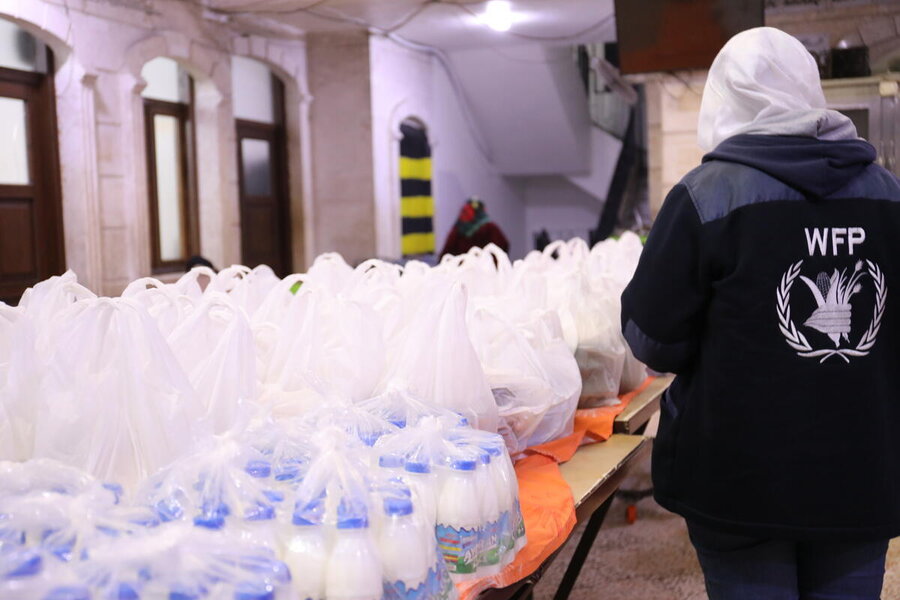 Backs of packed food ready to be distributed, a WFP staffer with her back to the camera, logo on her jacket