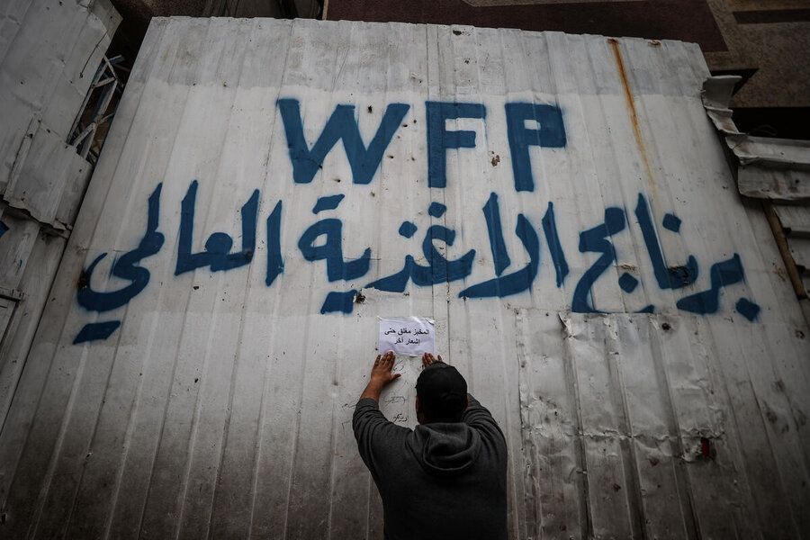 A hand painted WFP sign with, in Arabic, World Food Programme on the door of a bakery where a man posts a closure announcement on an A4 sheet