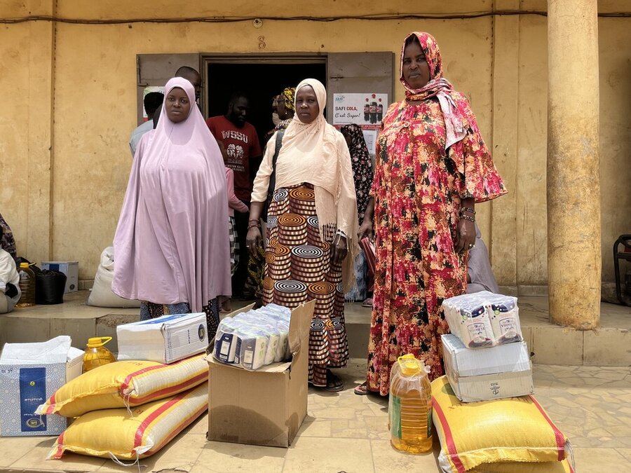 In Mali, three women at a food distribution point stand before packs of assistance