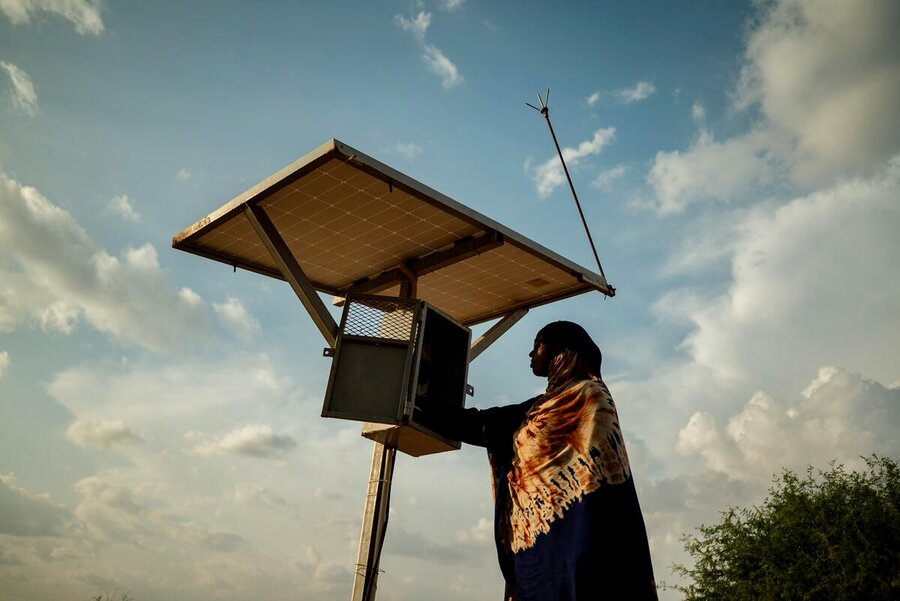 A woman in a headscarf stands next to a solar panel, backdropped by the sky. Photo: WFP/Arete/Edwin Ndeke