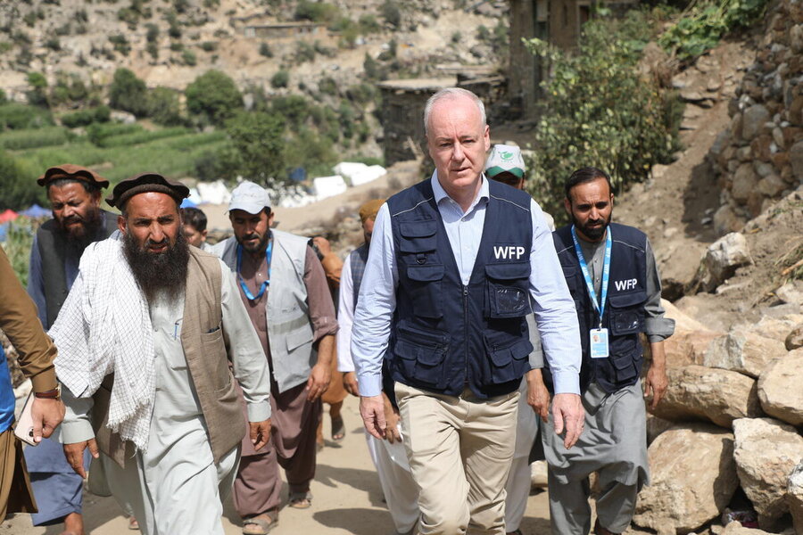 WFP Afghanistan Country Director John Aylieff, wearing a blue WFP jacket, strides up a hill with Afghan men and WFP staff. Photo: WFP/Arete/Muktar Nikrawa