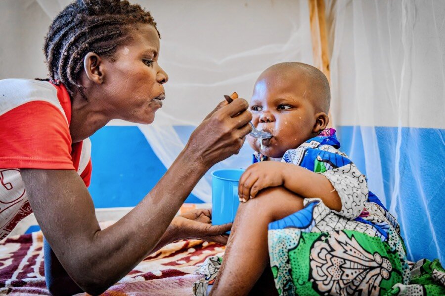 A woman in a red T-shirt spoons food into her baby's mouth. Photo: WFP/Charly Kasareka