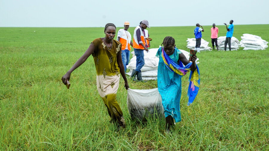 Two women drag a large white bag of WFP food away from a grassy airdrop zone in South Sudan's Upper Nile State. Photo: Peter Louis