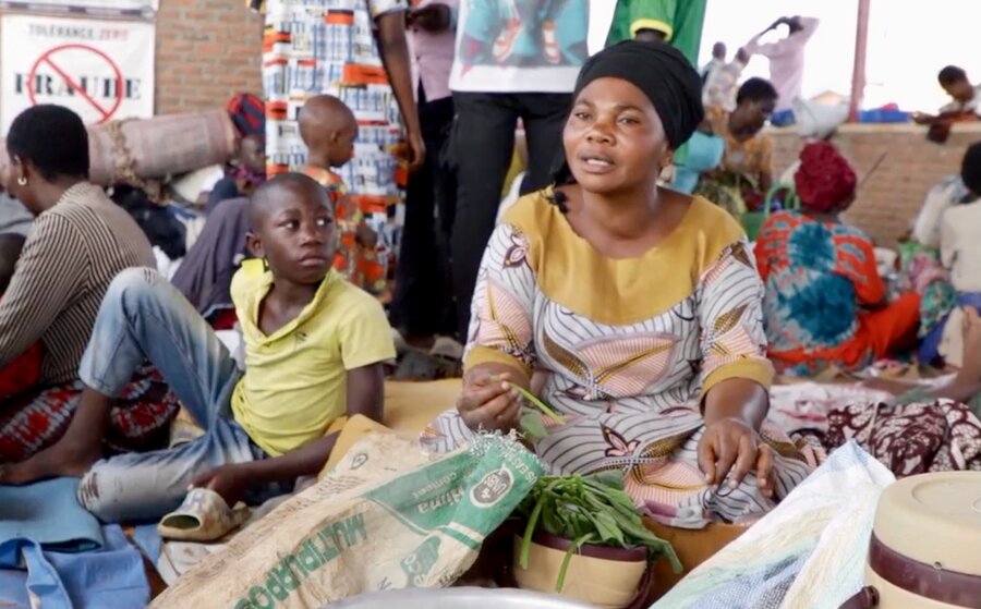 A woman sits on a mattress in a room surrounded by other people. Photo: WFP/Irenee Nduwayezu