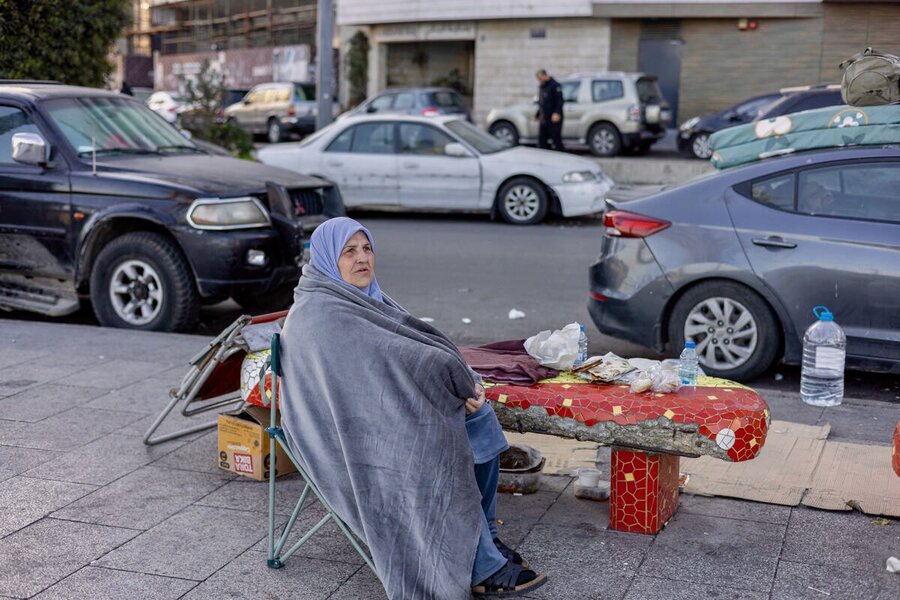 A displaced woman with a blue headscarf and blanket sits on a sidewalk in Beirut, with cars in the background. Photo: WFP/Alfredo Zuniga