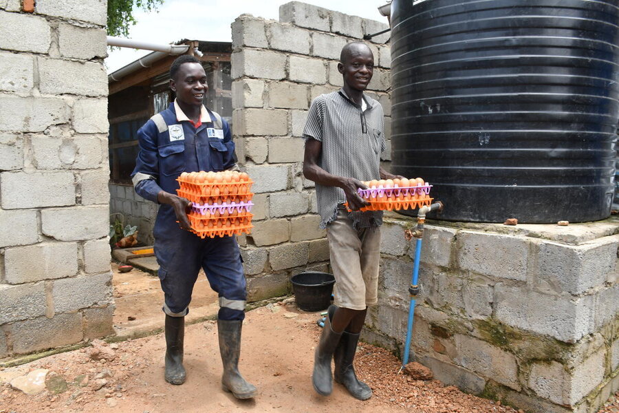 Two workers carrying containers of eggs emerge from a cement poultry house. Photo: WFP/Machrine Birungi